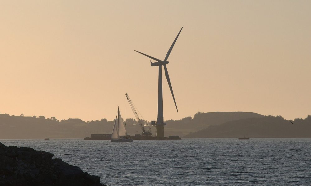 A large wind turbine assembled beside a fjord under a wide sky