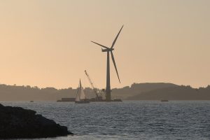 A large wind turbine assembled beside a fjord under a wide sky