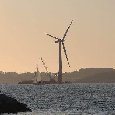 A large wind turbine assembled beside a fjord under a wide sky